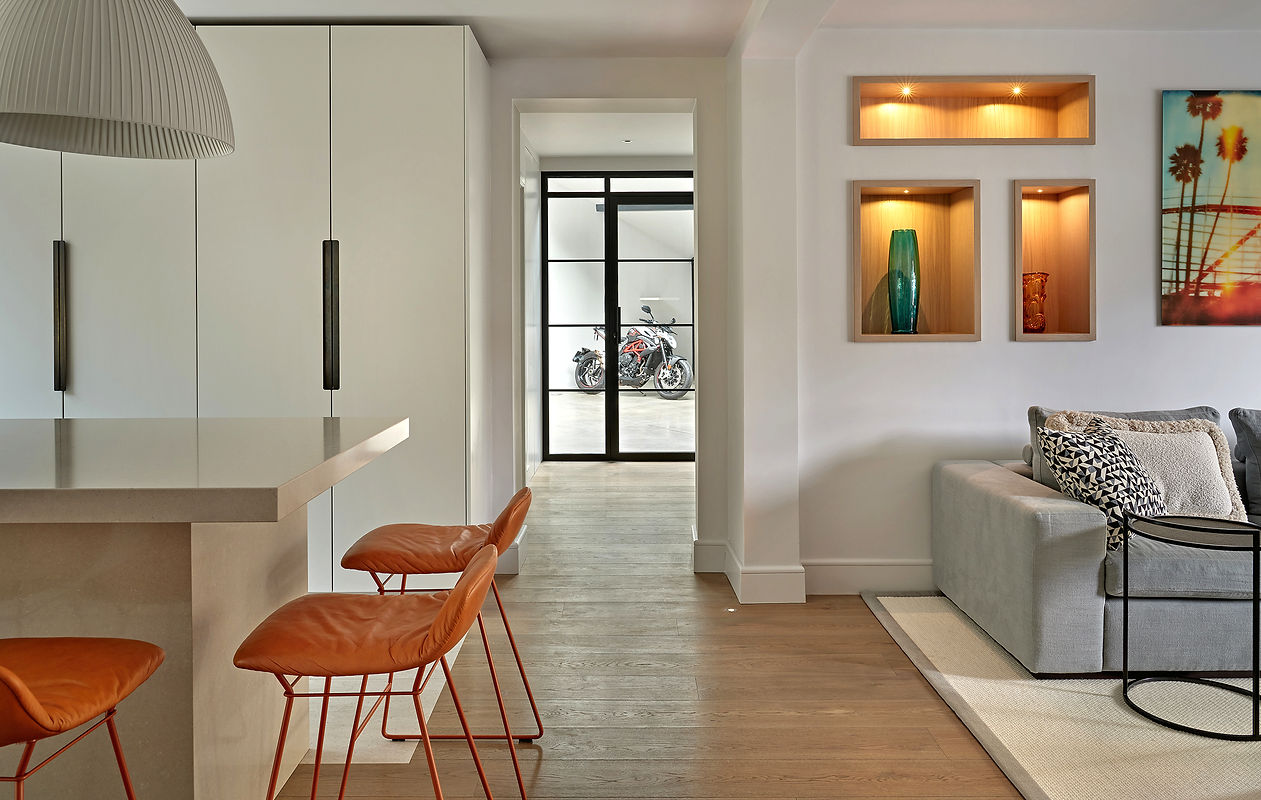 Modern open-plan kitchen and living area with stone island, leather bar stools, bespoke display niches and glass doors to garage, contemporary family home interior