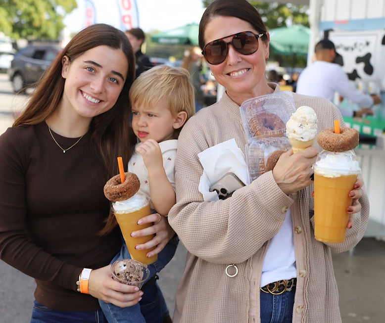 Two women and a toddler holding milkshakes topped with donuts