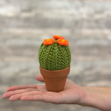 Crocheted cactus with orange flowers in a terracotta pot, sitting on an open hand.