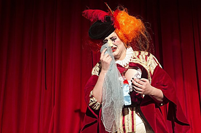 A white woman dressed in Elizabethan attire performs a cabaret act, dramatically crying into a handkerchief