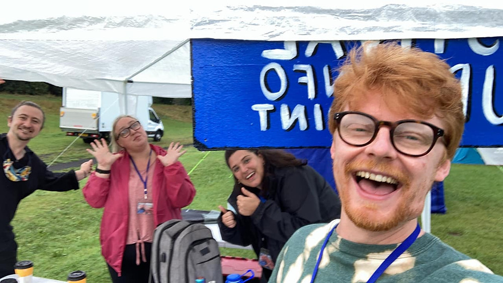 Four smiling production team members celebrate that the sun has come out under a tent in a field.