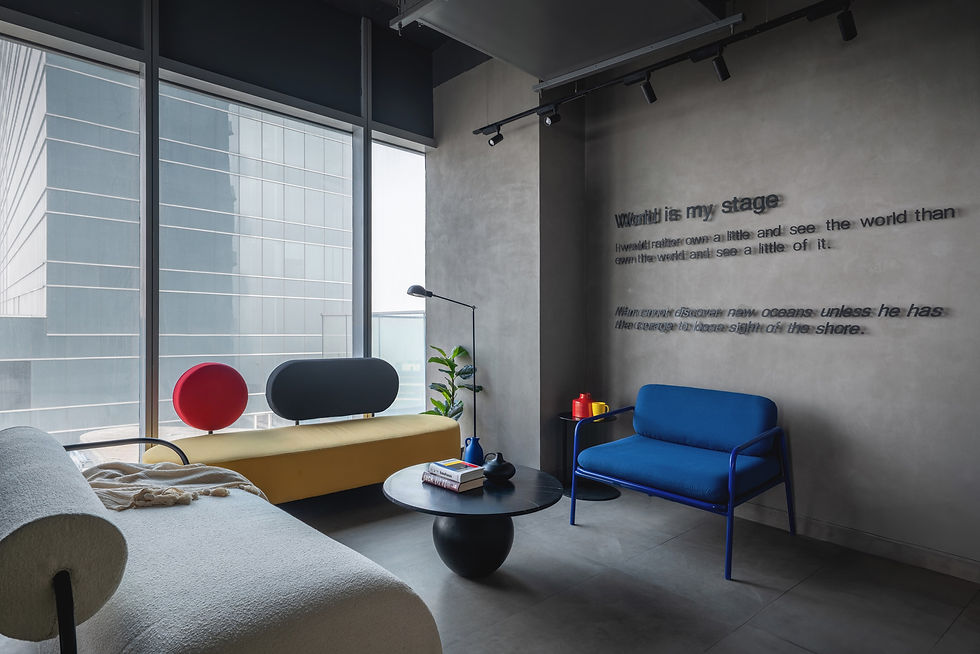 Modern room with a yellow chaise, blue chair, and round table. Red and yellow decor on the table. Text on the wall reads "World is my stage."