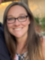 Smiling woman with glasses in a floral dress outdoors, warm lighting, tree and grasses in the background, creating a cheerful mood.