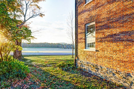 Sunset light over the brick wall of Old Reed Homestead, overlooking open fields and autumn trees in Honeoye, NY