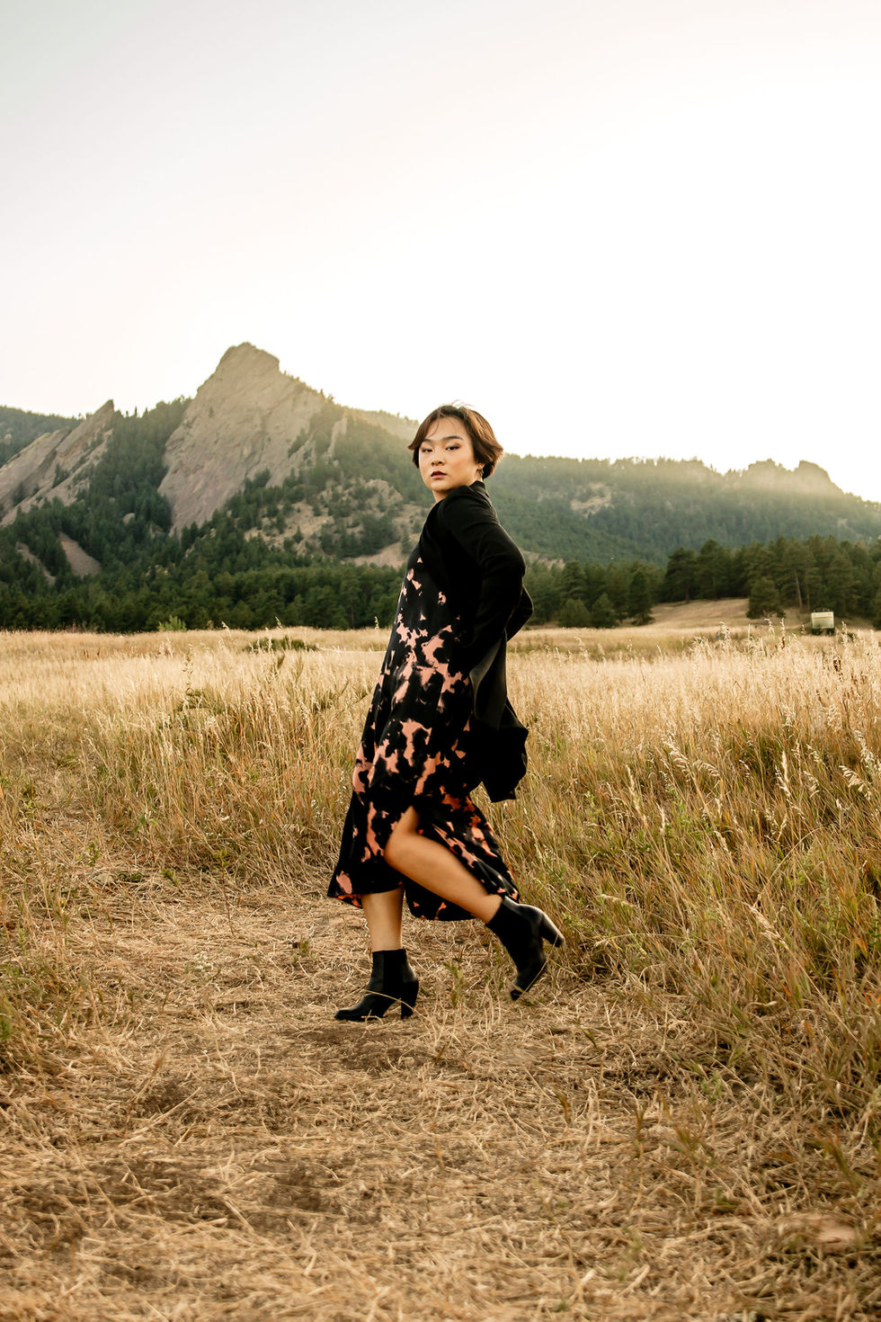 a woman in a black dress is walking in a field with mountains in the background