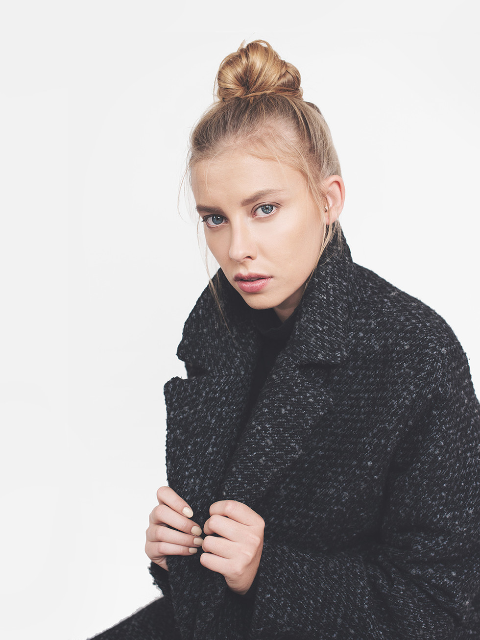 Young woman with blonde hair wearing dark grey coat on white background.