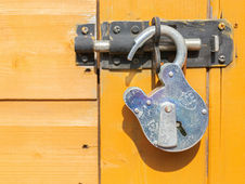 Weathered silver padlock secures a black latch on a bright yellow wooden door, with ACE visible.