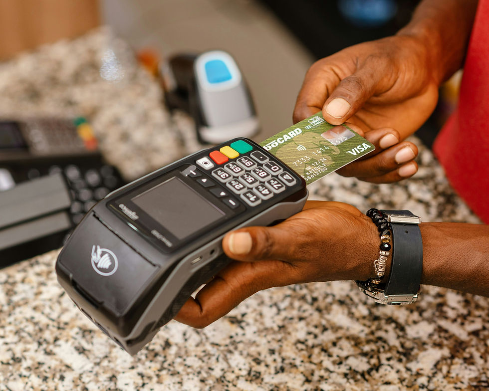 Hands holding a Visa card and a payment terminal over a granite counter, preparing for a contactless transaction.