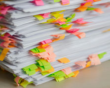 Stack of white papers covered with colorful sticky notes in pink, green, orange, and yellow on a desk, suggesting busy office work