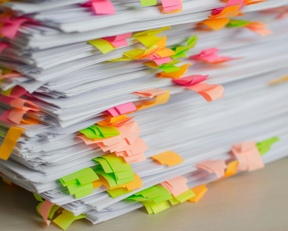 Stack of white papers covered with colorful sticky notes in pink, green, orange, and yellow on a desk, suggesting busy office work