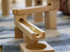 Wooden marble run on a blue-striped rug. A yellow marble is rolling down the track, creating a playful and engaging scene.