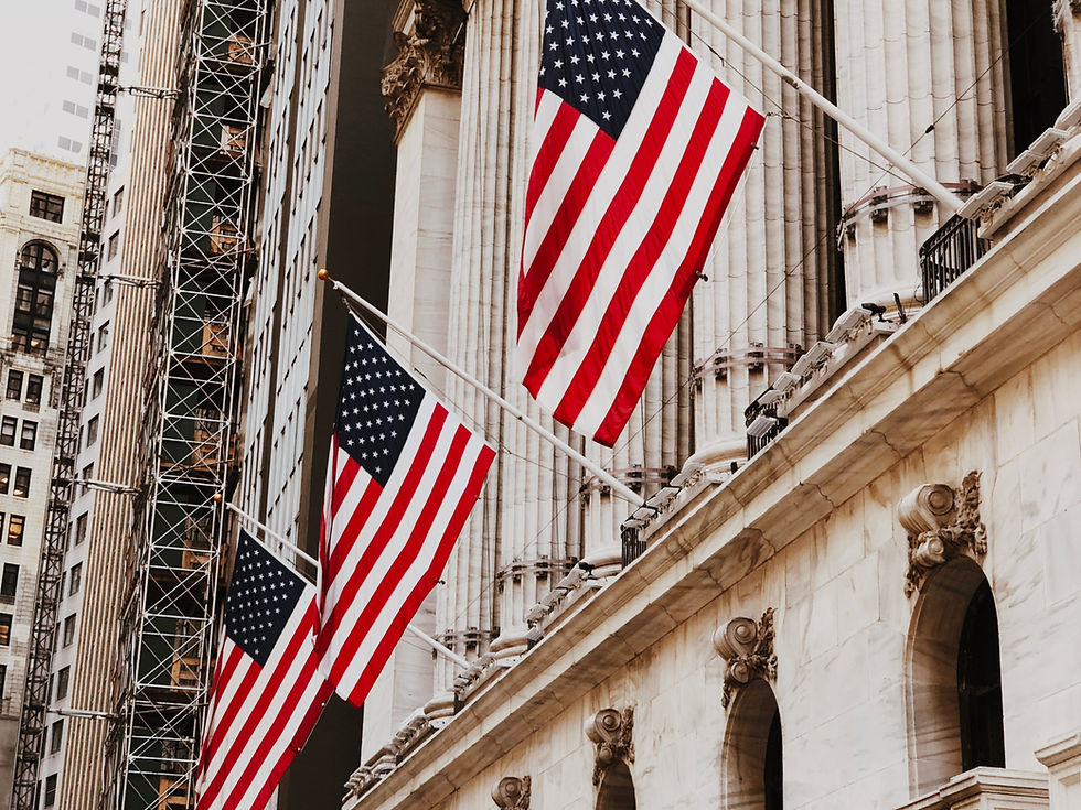 American flags wave on a historic white stone building with columns, set against modern city architecture under a clear sky.