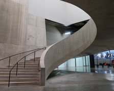 Concrete spiral staircase in a modern interior, with wall text reading Galleries Terrace Shop Bar and cool fluorescent lighting.