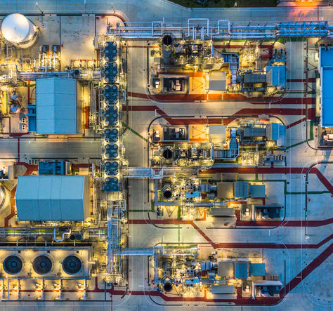 Overhead view of an illuminated industrial plant with tanks, pipes, and blue-roofed buildings.