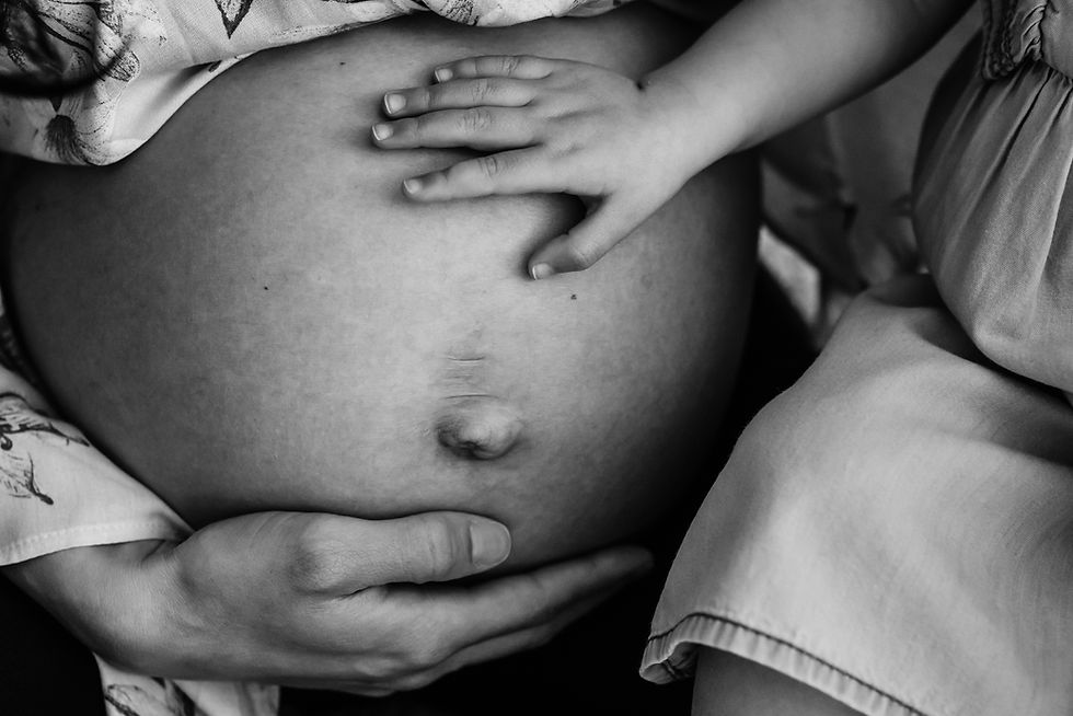 Pregnant woman's belly touched by a child's hand in black and white colour