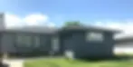 Newly painted dark grey brick bungalow exterior with white trim, manicured lawn, and clear blue sky
