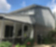 Freshly painted dark grey house siding and covered porch exterior with brick foundation and garden