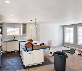 Kitchen and dining room interior mid-project with white cabinets, painter's drop cloths on the floor, and a garbage bin during active painting