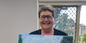 A woman holding up her finished painting of a field of flowers