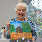 A woman holding up her finished painting of a field of flowers