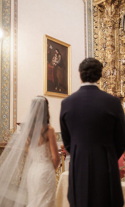 Novios de espaldas durante ceremonia religiosa en iglesia con retablo dorado