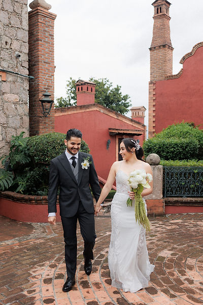 Pareja de novios caminando de la mano en boda al aire libre con arquitectura colonial