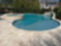 A beautiful concrete inground pool built by Caliber Custom Pools. The image displays the results of a Marmiro Travertine pool deck, with an integrated water feature that adds a soothing waterfall sound.