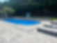 A beautiful concrete inground fiberglass pool built by Caliber Custom Pools. The image displays the results of a Paver Pool Deck, with an integrated retaining wall that enhances the landscape of the property. River rock was used for the French drain system as a sustainable method to help facilitate the property drainage.