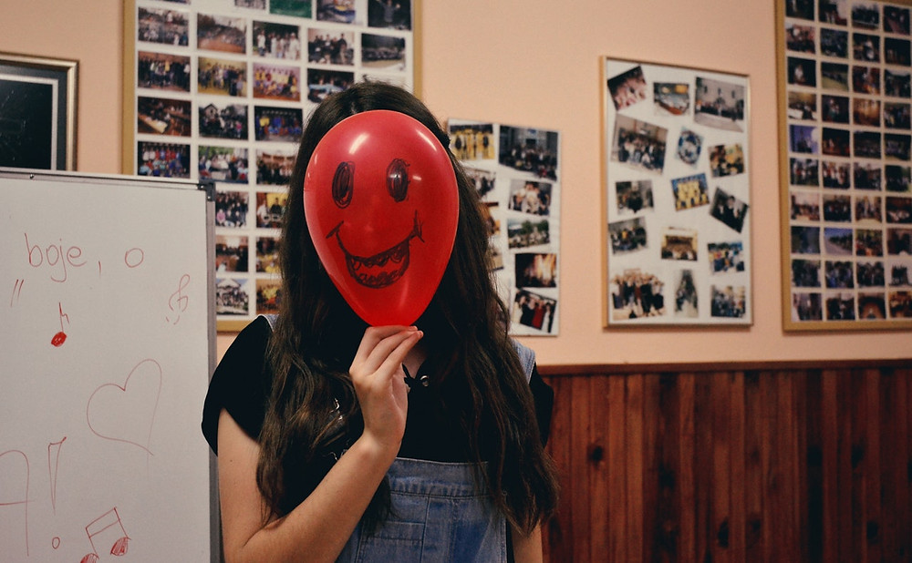 Woman with smiling balloon in front of her face in a classroom