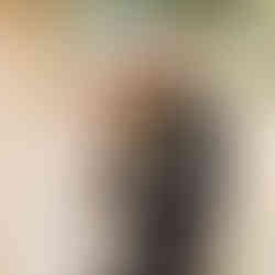 A bride in white stands with a groom in military dress an an outdoor wedding, both are smiling in the direction of their guests