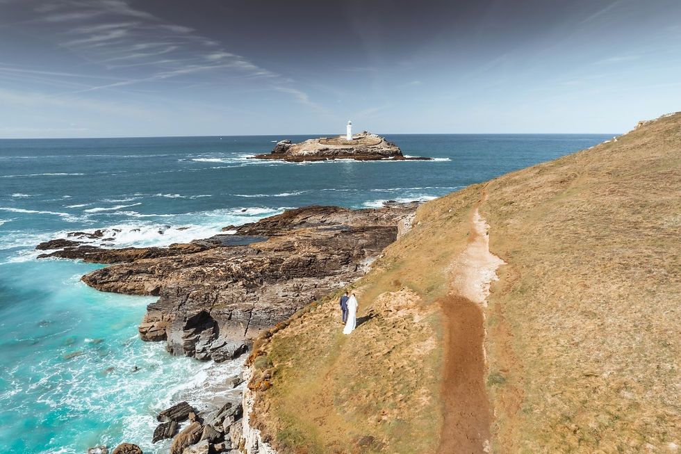A bride and groom walk with Godrevy Lighthouse in view