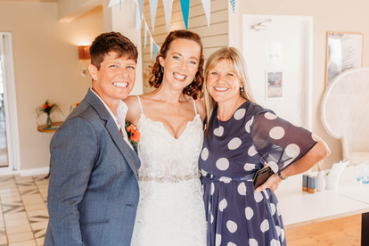 Three women stand arm in arm at a wedding ceremony -ttwo brides and the officiant - all are smiling