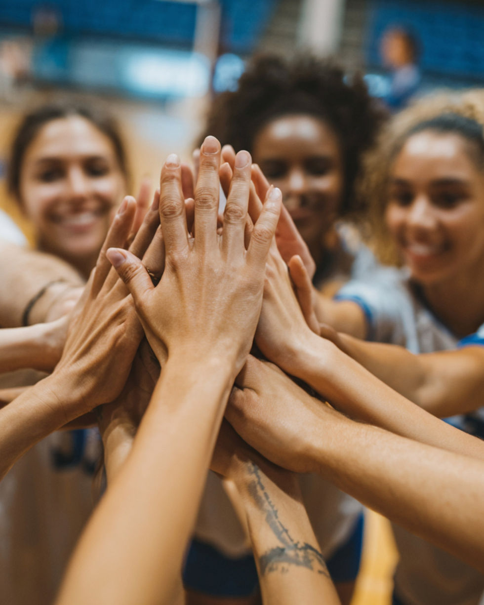 Girls volleyball players coming together as a team joining hands.