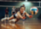 A girls volleyball player diving after a volleyball.