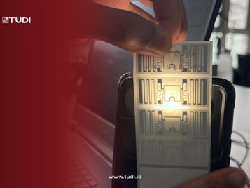 Foto RFID Chip yang di beri cahaya highlight dengan gradasi merah dan logo tudi di pojok kiri atas.