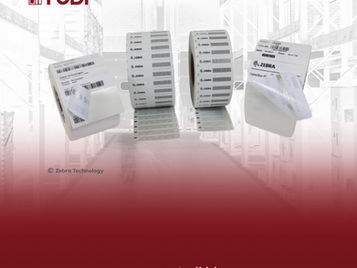 Label rolls hover over a blurred warehouse background. Red gradient with "TUDI" and "www.tudi.id" text. Multipe "Zebra" logos visible.