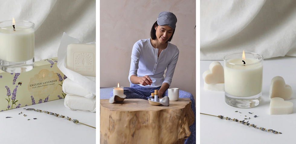 Woman in gray cap, sitting by a log table with candle, essential oils. Nearby, lavender soap and heart-shaped soaps are displayed. Peaceful vibe.