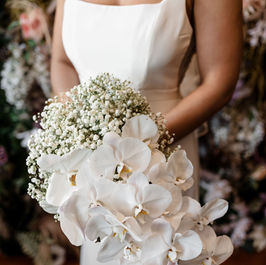 Bride in white dress holding white cascading baby's breath and orchid bouquet, wedding flowers.