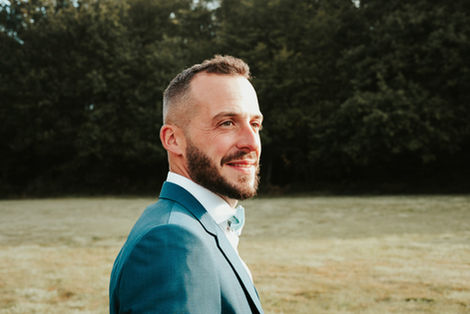 Portrait souriant du marié en costume, lumière naturelle et fond flou pour une photographie élégante et intemporelle.