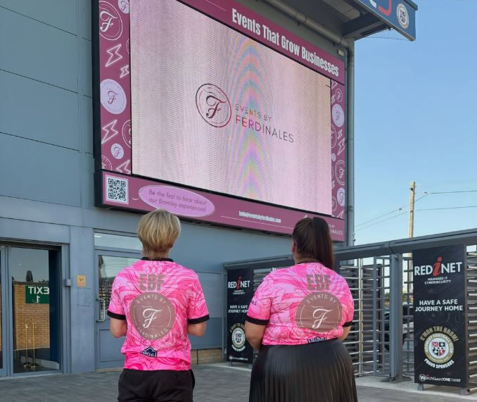 EBF team in branded football shirts standing in front of digital screens at Bromley FC stadium