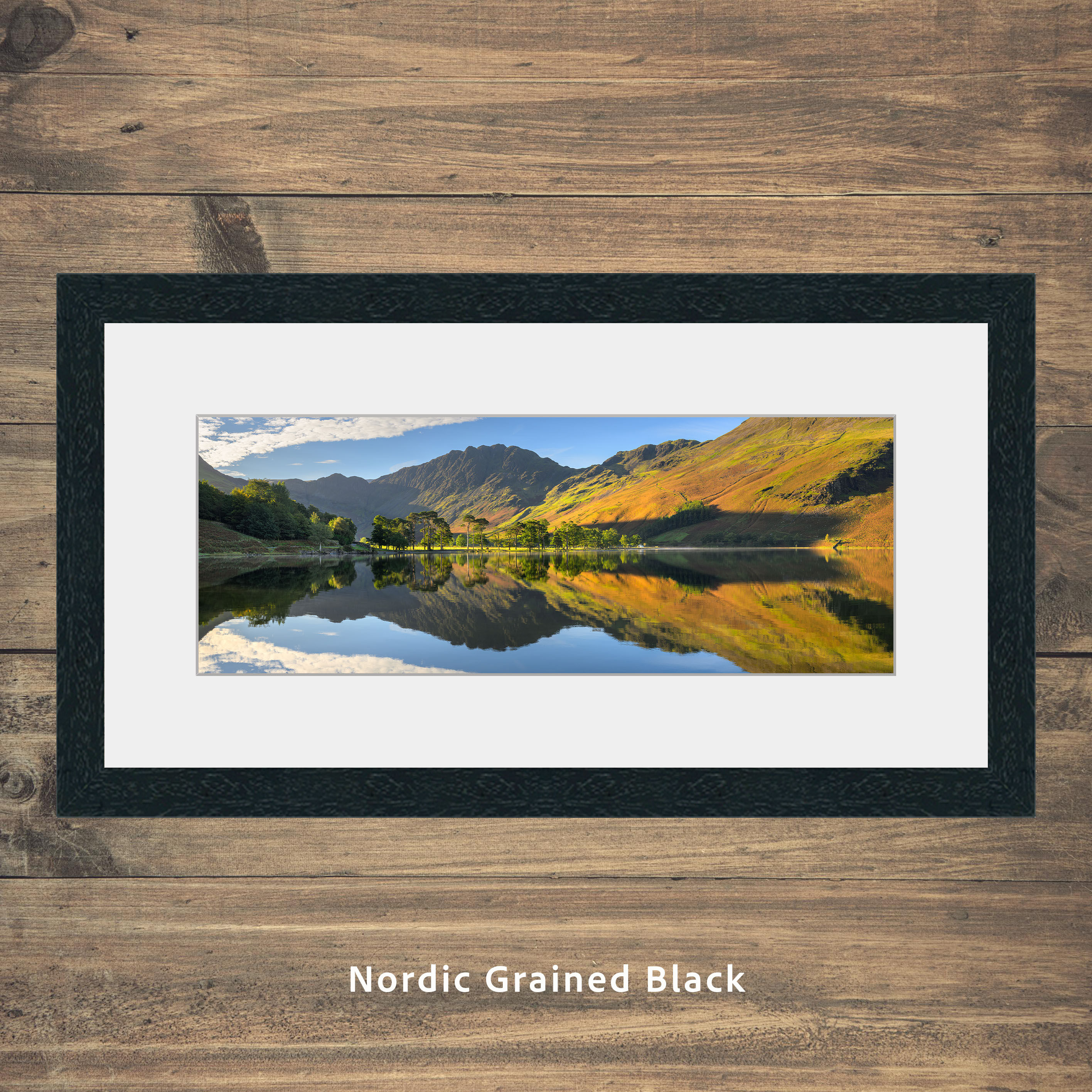 Beautiful autumn colours reflecting in a calm panoramic view of Buttermere with crisp blue skies, Lake District, UK.