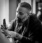 Tattoo artist and shop owner, Jazz. He's focused on tattooing a client.