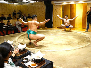 東京淺草室內相撲表演場地中，前相撲力士在土俵上示範相撲動作，觀眾一邊用餐一邊欣賞表演。