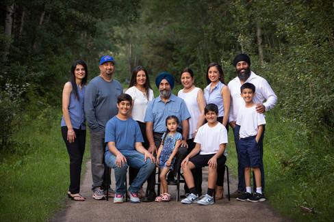 A family of eleven poses smiling on a forest path, wearing casual blue and white clothing. Lush green trees surround them, creating a serene setting.