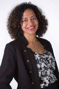 Smiling woman with curly hair in a black jacket and floral top, set against a plain white background, exuding a confident and friendly mood. Viewpoint Photography Edmonton