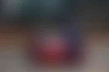 Young man in blue suit stands confidently beside a red car in a city rooftop parking lot. Glass buildings in background, "Deloitte" sign visible. Grad photo session Edmonton.