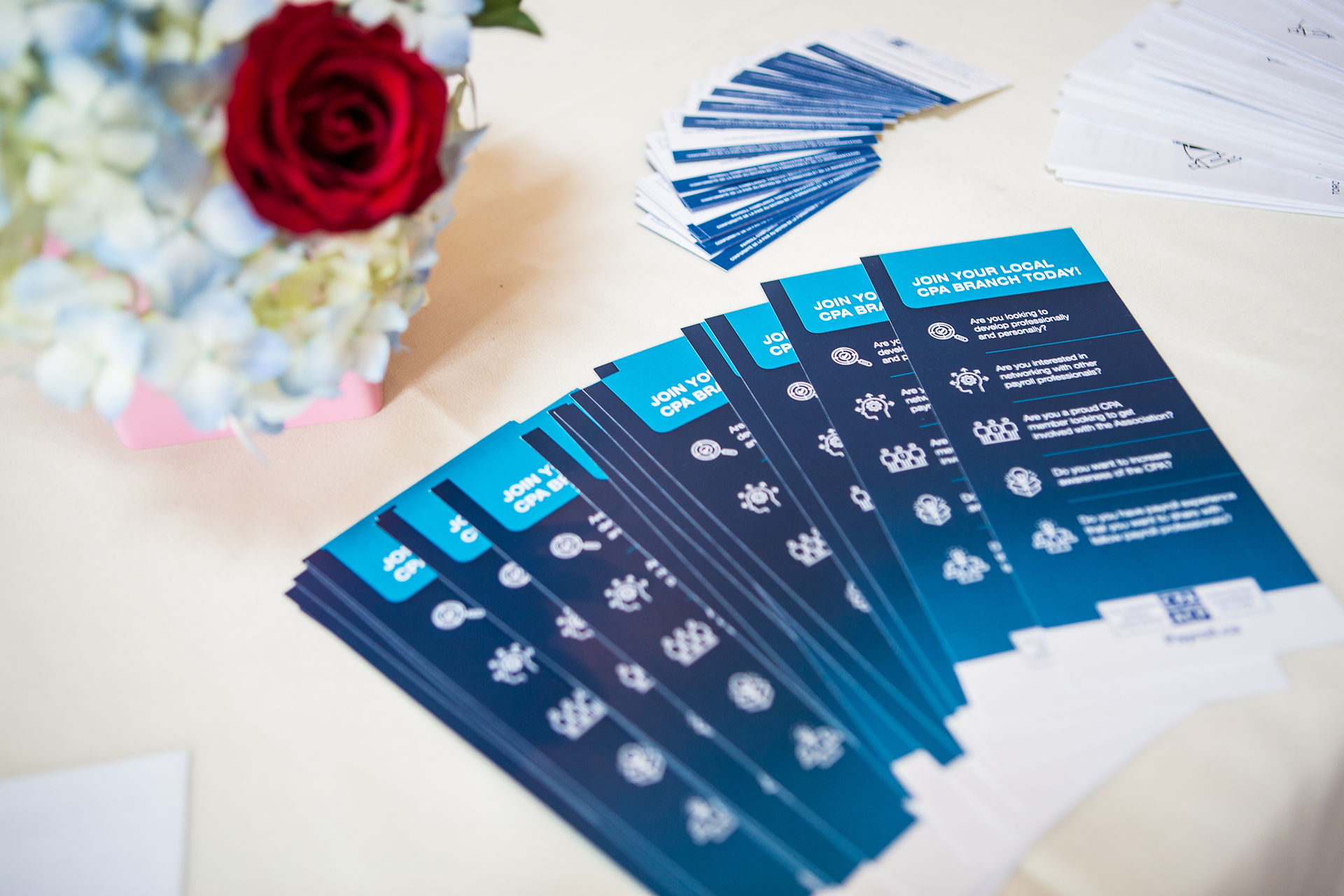 Blue brochures with "Join Your Local CPA Branch Today" text on a table, next to a bouquet with a red rose and light blue flowers. Canadian Payroll Association. Event Photographer Edmonton.