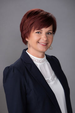 Smiling woman with short auburn hair in a navy blazer and white lace top against a gray background, exuding a professional vibe. Viewpoint Photography Edmonton