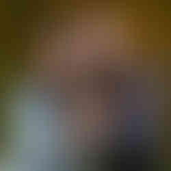 Two smiling girls holding a small dog outdoors. One wears a jean jacket, the other a blue sweatshirt. Autumn foliage in the background.