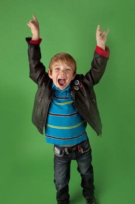 Child in a black leather jacket and blue striped shirt, cheering with raised arms against a green background, expressing excitement. Children's photography Edmonton